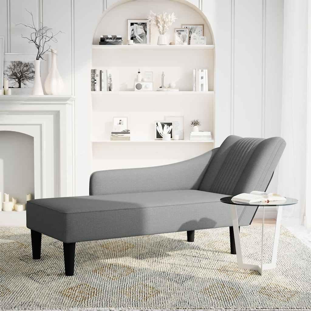 A grey chaise lounge is placed on a patterned rug in a room with a fireplace and shelves.
