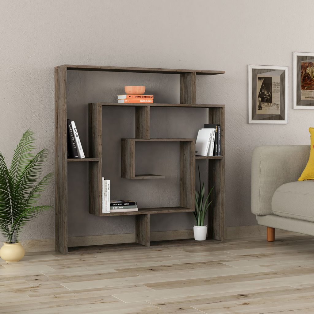 A modern, modular bookshelf is displayed against a plain wall, with a potted plant to the left and a portion of a sofa with a yellow cushion to the right.