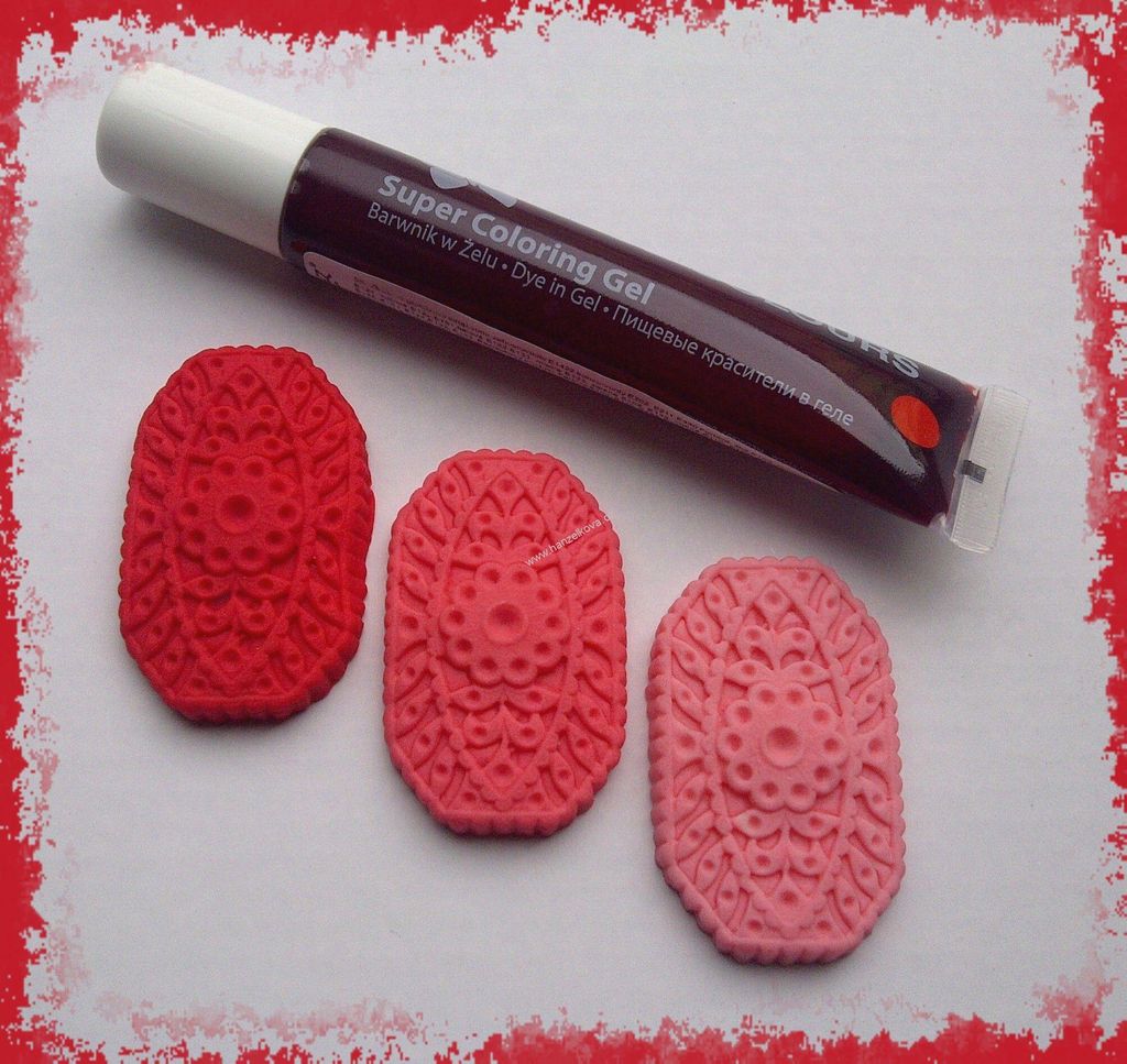 A tube of gel food coloring and three decorative elements made from dough or clay, colored in shades of red and pink.