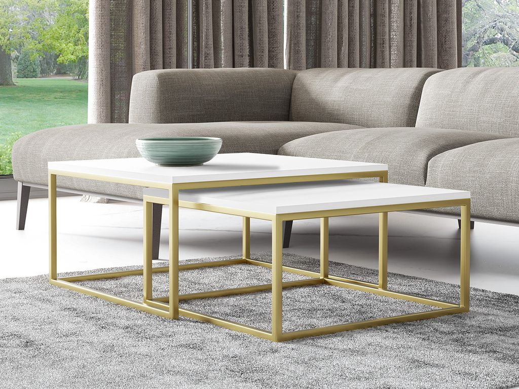 Two nesting coffee tables with white tops and gold metal frames are placed on a gray rug in front of a sectional sofa. A green bowl sits on the larger table.