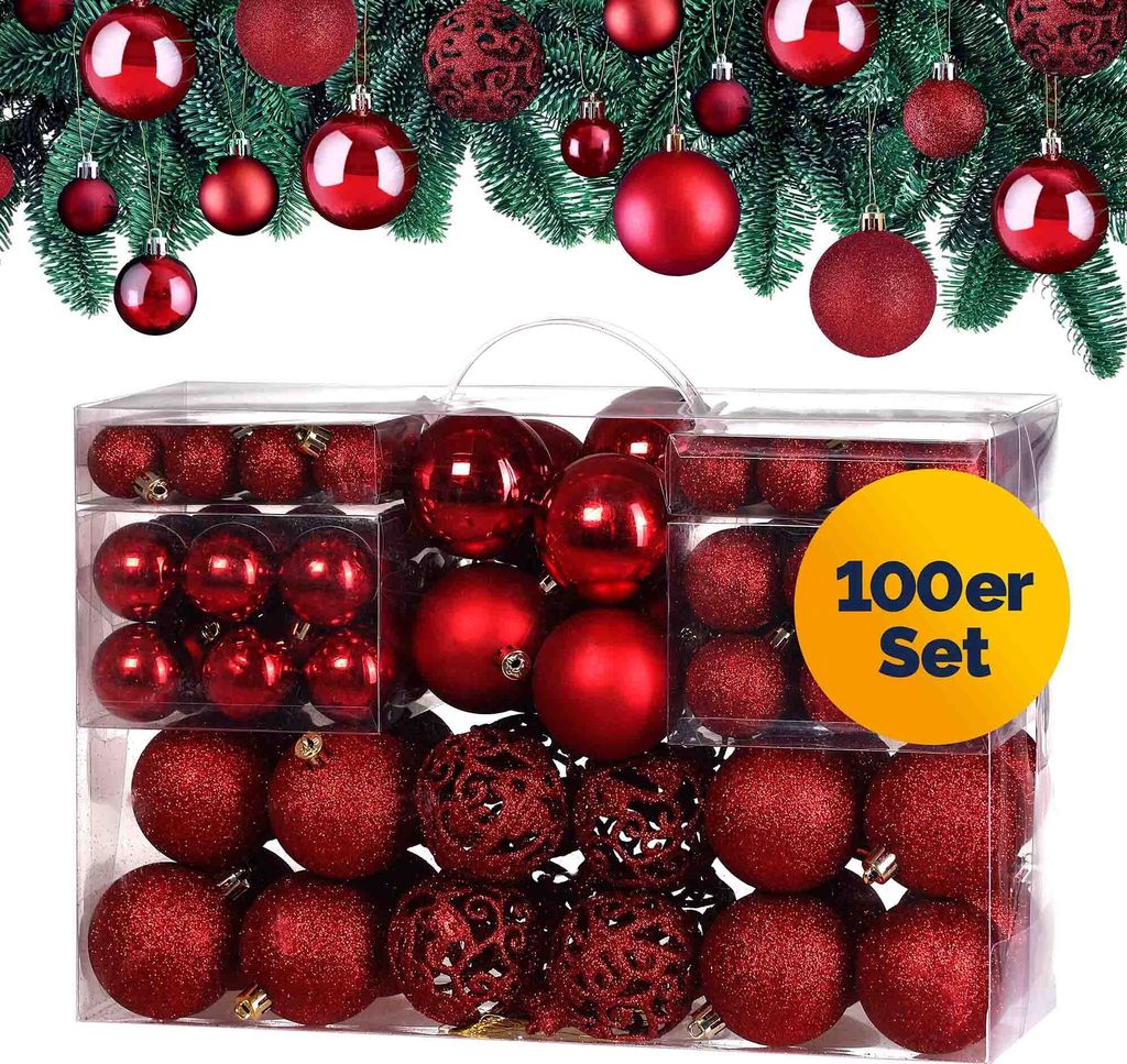 A set of red Christmas ornaments in a clear plastic box, with a festive green garland in the background.