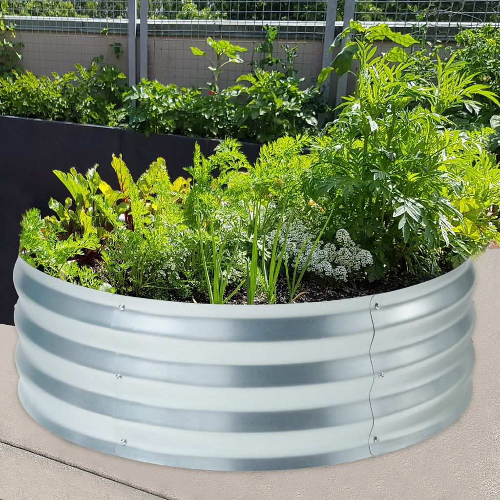 A raised garden bed filled with various plants, including carrots and leafy greens, sits on a patio.