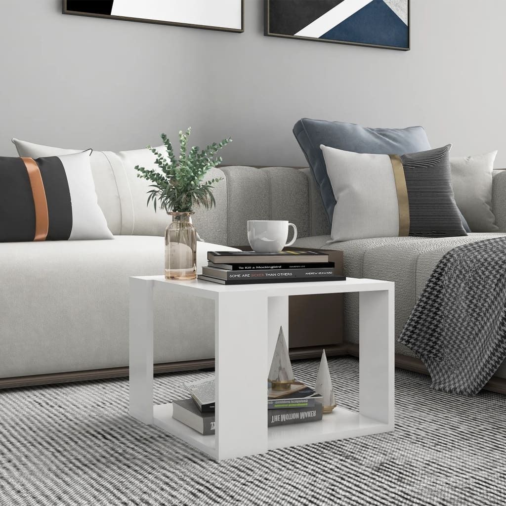 A white side table with books and a vase of greenery on it, placed next to a sofa in a living room.