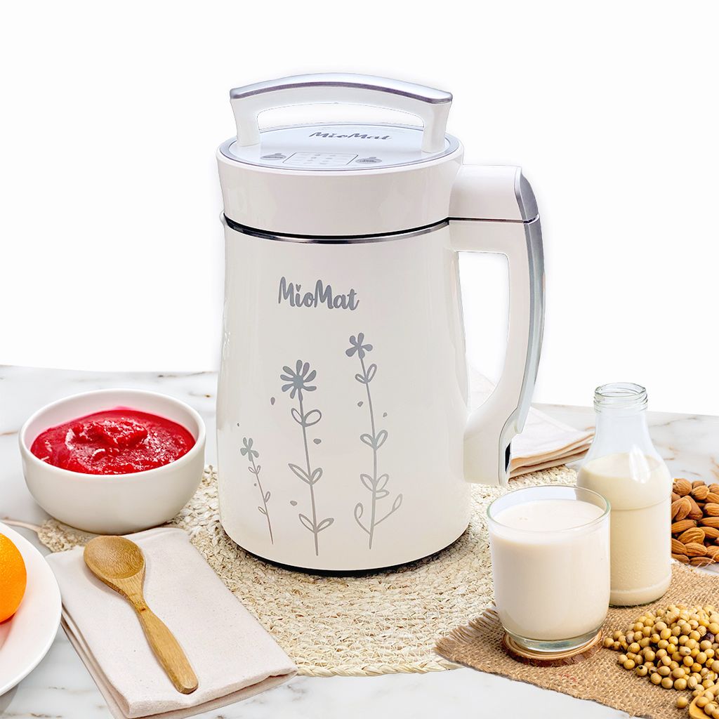 A white MioMat soy milk maker is presented on a marble countertop with various ingredients and finished products, including a bowl of crushed strawberries, a glass of soy milk, a bottle of soy milk, almonds, and soybeans.