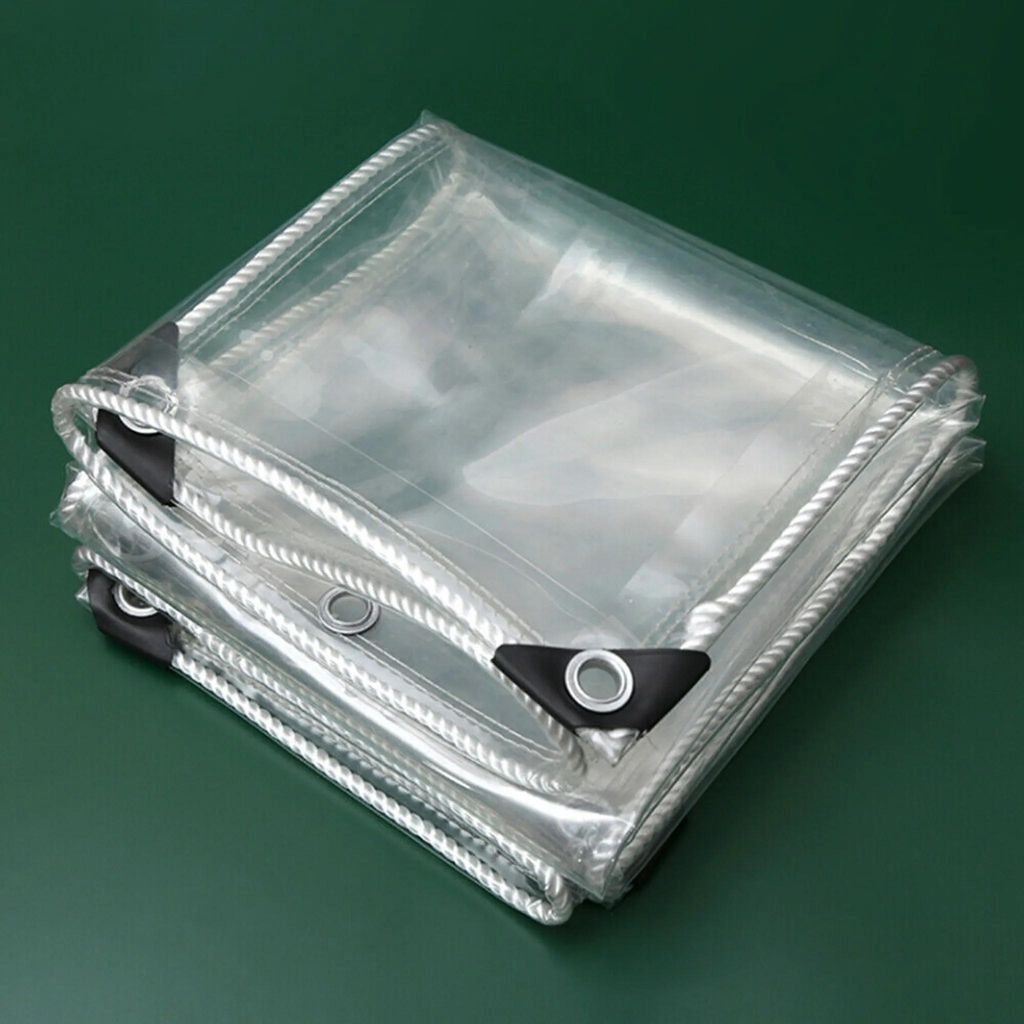 A folded clear PVC tarp with reinforced corners and rope edging, placed on a green surface.
