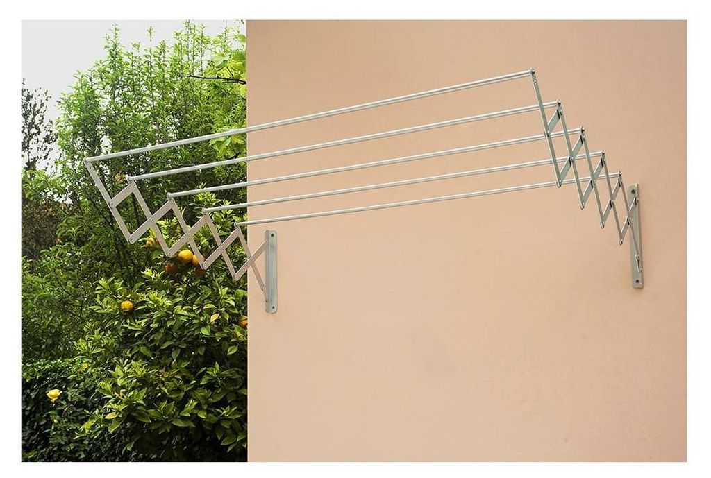 A retractable clothesline mounted on a wall, with trees and foliage in the background on the left side.