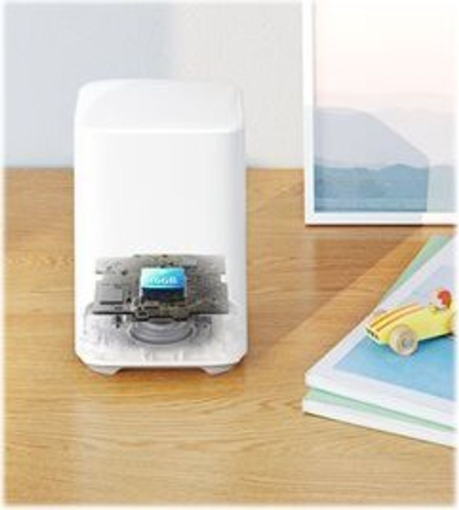 A white smart home device with its internal components exposed, placed on a wooden surface next to a stack of books and a framed picture.