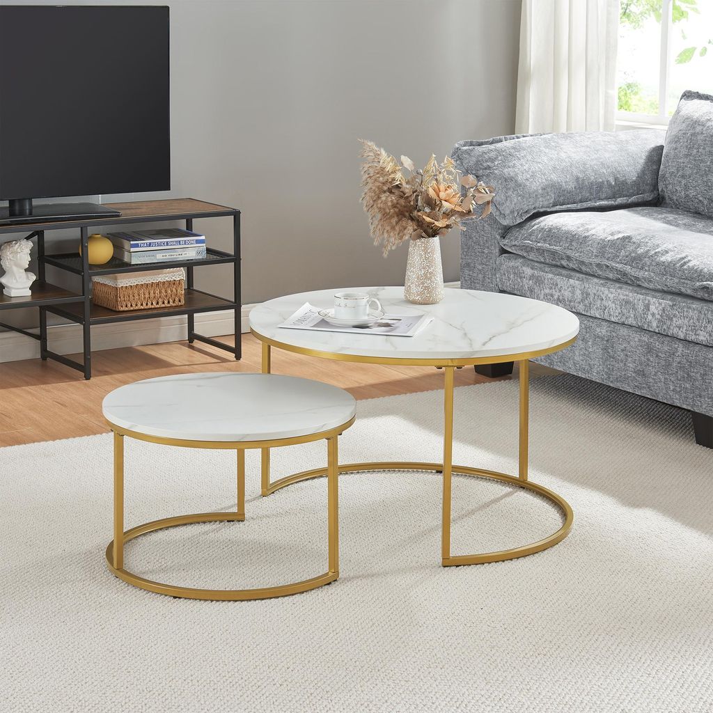 A living room scene featuring a nesting coffee table set with a marble-like top and gold metal legs, placed on a rug next to a sofa.