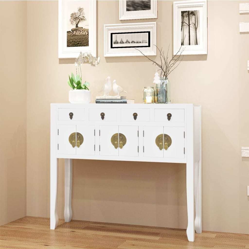 A white console table with brass hardware is displayed against a light beige wall, with framed artwork above.
