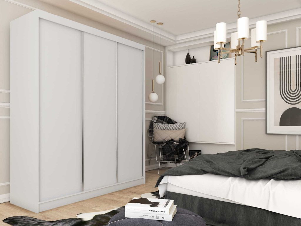 A bedroom scene featuring a large white wardrobe, a bed with dark bedding, a chair with cushions, and decorative elements on the wall.