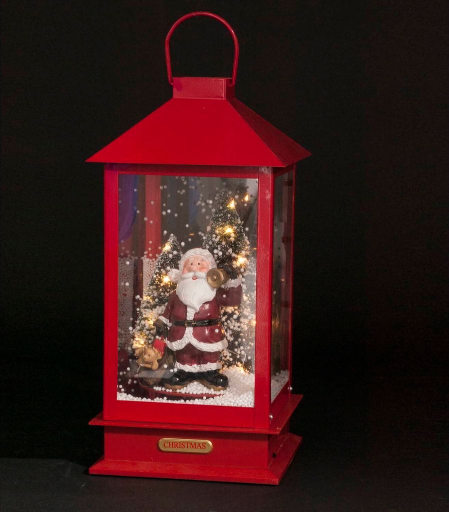 A red lantern with a Santa Claus figurine inside, illuminated by LED lights and surrounded by artificial snow and miniature Christmas trees.