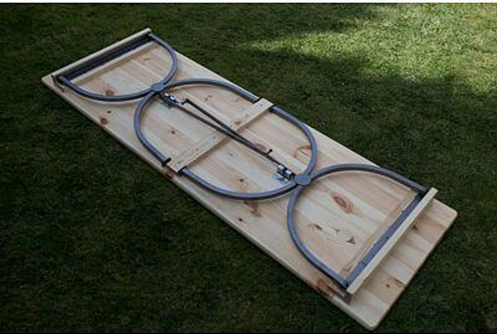 A wooden picnic table with metal legs folded and lying on grass.