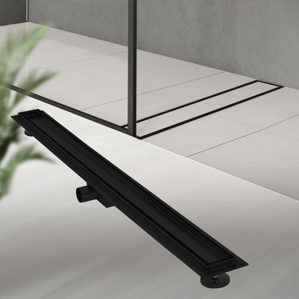 A black linear shower drain is shown on a tiled floor in a modern bathroom setting.