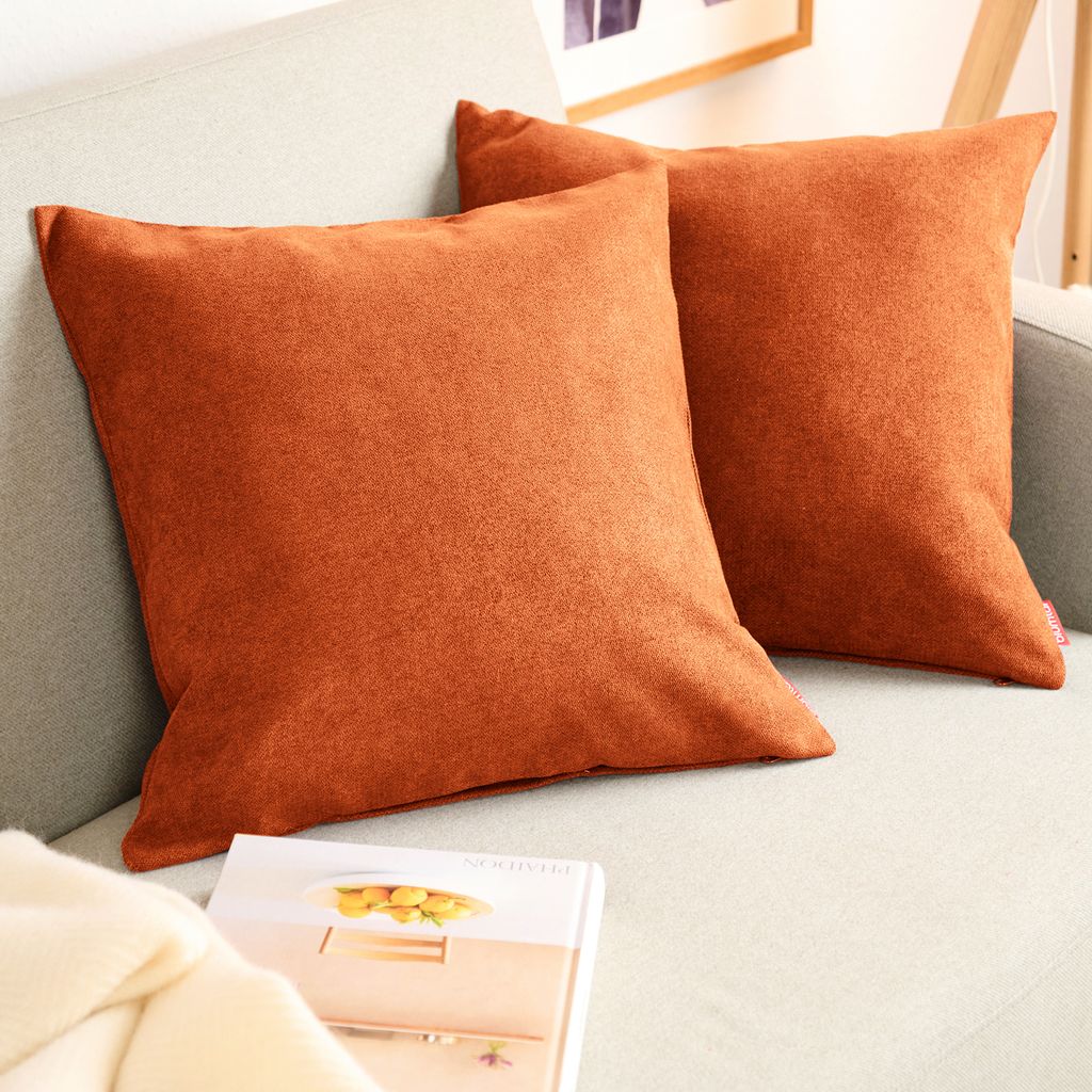 Two orange throw pillows are placed on a light gray sofa.