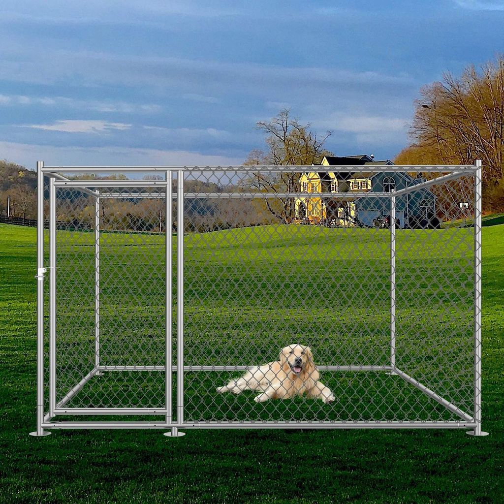 A dog is lying inside a metal dog kennel in a grassy field with a house in the background.