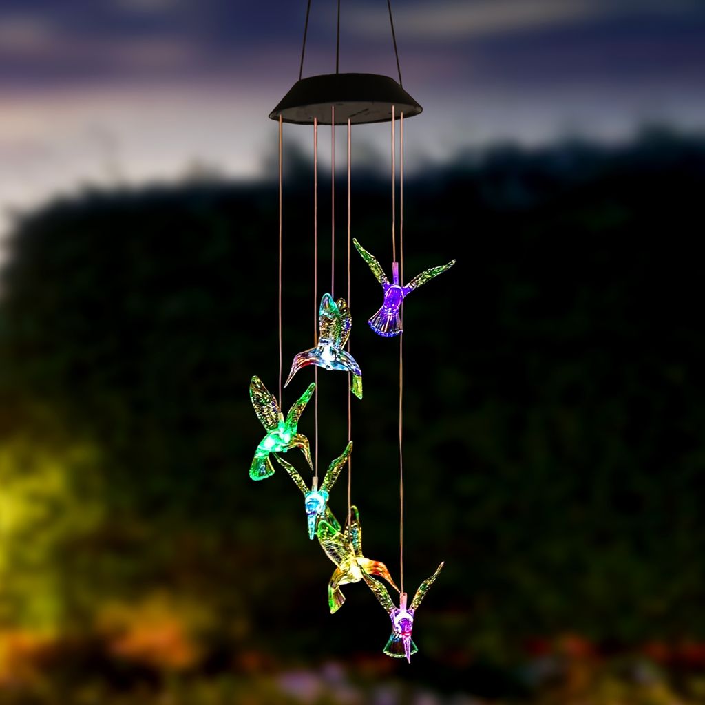 A solar-powered wind chime with hummingbird-shaped lights hanging outdoors at dusk.