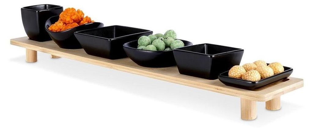 A set of black ceramic bowls filled with snacks, arranged on a light brown bamboo tray with legs.