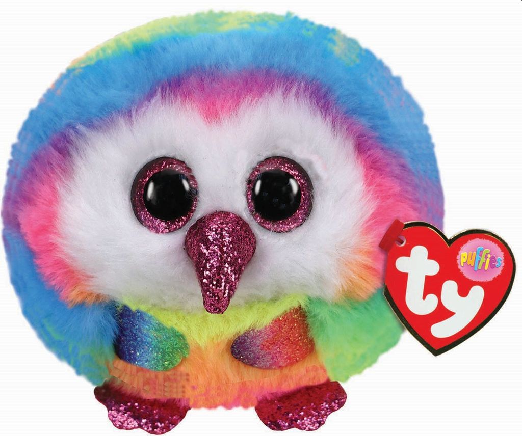 A close-up studio shot of a rainbow-colored plush owl toy with large glittery eyes and a glittery beak. A red heart-shaped TY tag is attached to its side.