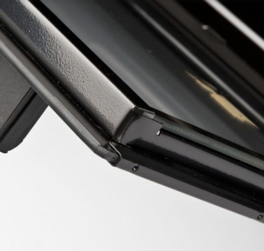 A close-up view of the corner of a black appliance, possibly a oven or grill, showing the textured metal frame and a glass surface.