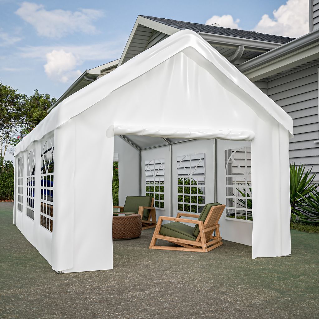 A white party tent set up next to a house, with outdoor furniture inside.