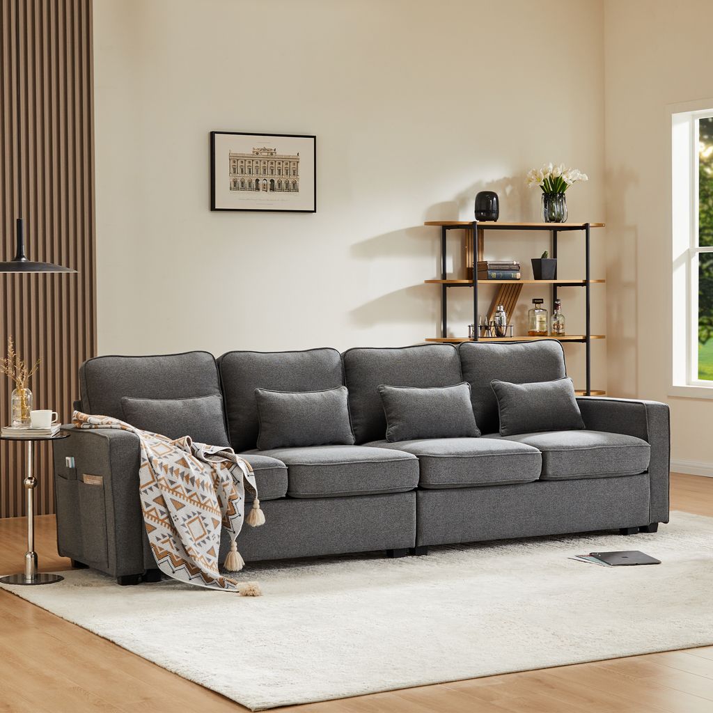 A dark gray sofa with throw pillows and a blanket is placed on a light-colored rug in a living room setting.