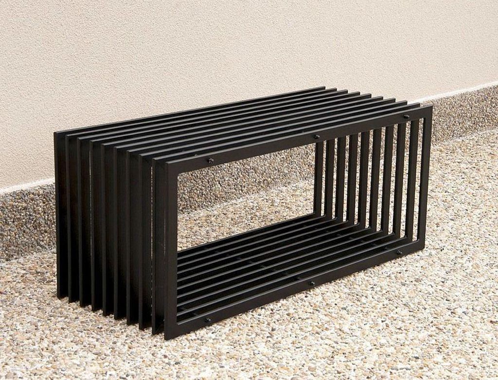 A black metal bench is placed on a gravel and concrete surface next to a light-colored wall.