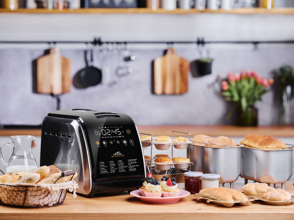 A kitchen counter with a bread maker and various baked goods, including cupcakes and bread rolls.