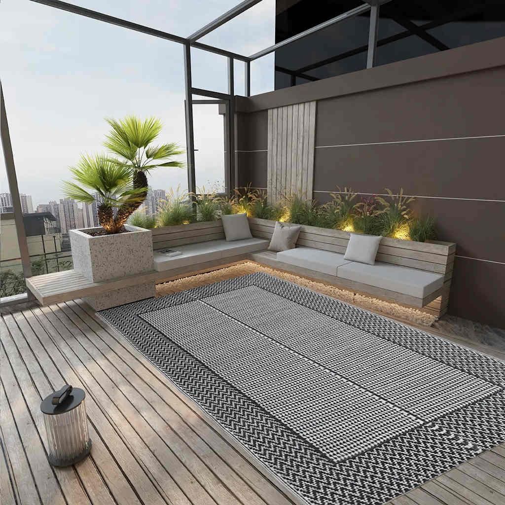 A modern outdoor patio with a rug, seating, and plants.