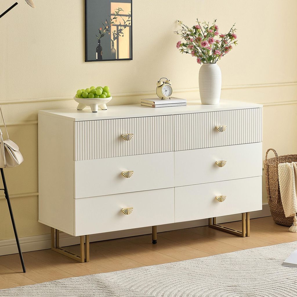 A white dresser with gold accents is shown in a room setting, with decorative items on top.