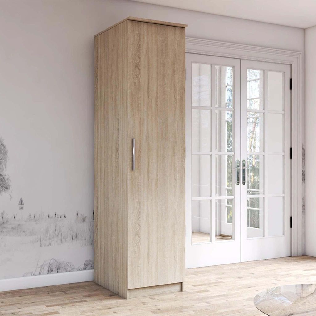 A tall, narrow cabinet with a light wood grain finish is placed against a wall with a decorative mural and next to a set of double doors. The floor is made of light wood planks.