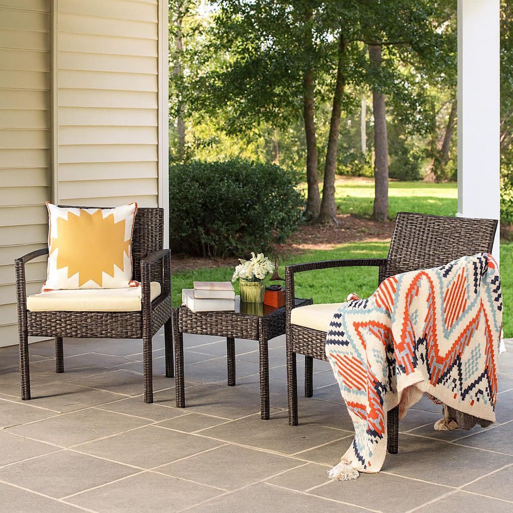 Two chairs and a small table on a patio with trees and bushes in the background.
