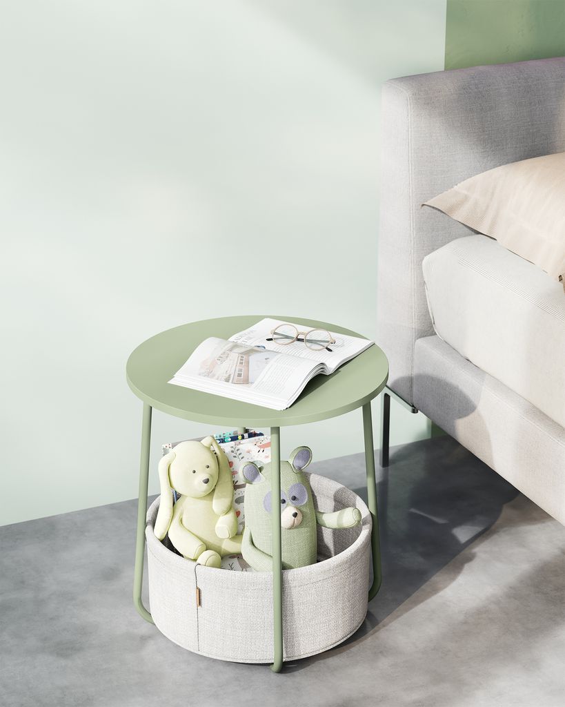 A round green side table with a storage basket underneath holding stuffed toys, next to a bed.