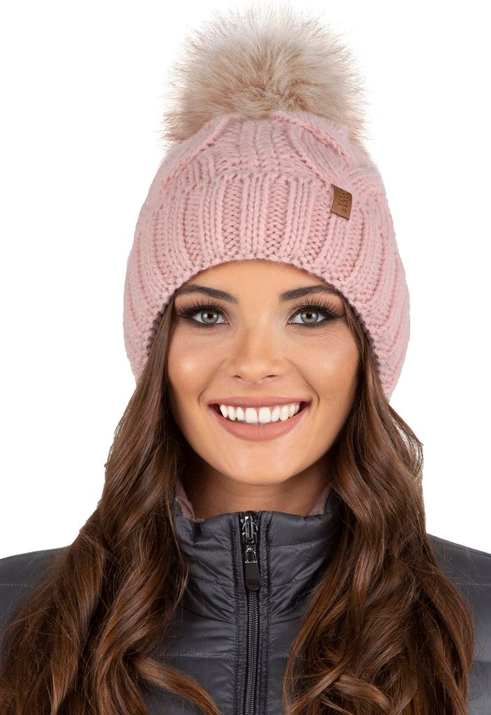 A woman wearing a pink knitted beanie with a fluffy pom-pom.