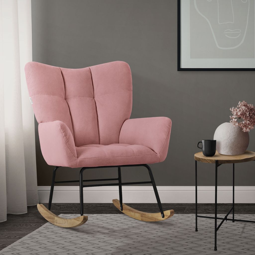 A pink rocking chair in a living room setting, next to a small side table with a vase and mug.
