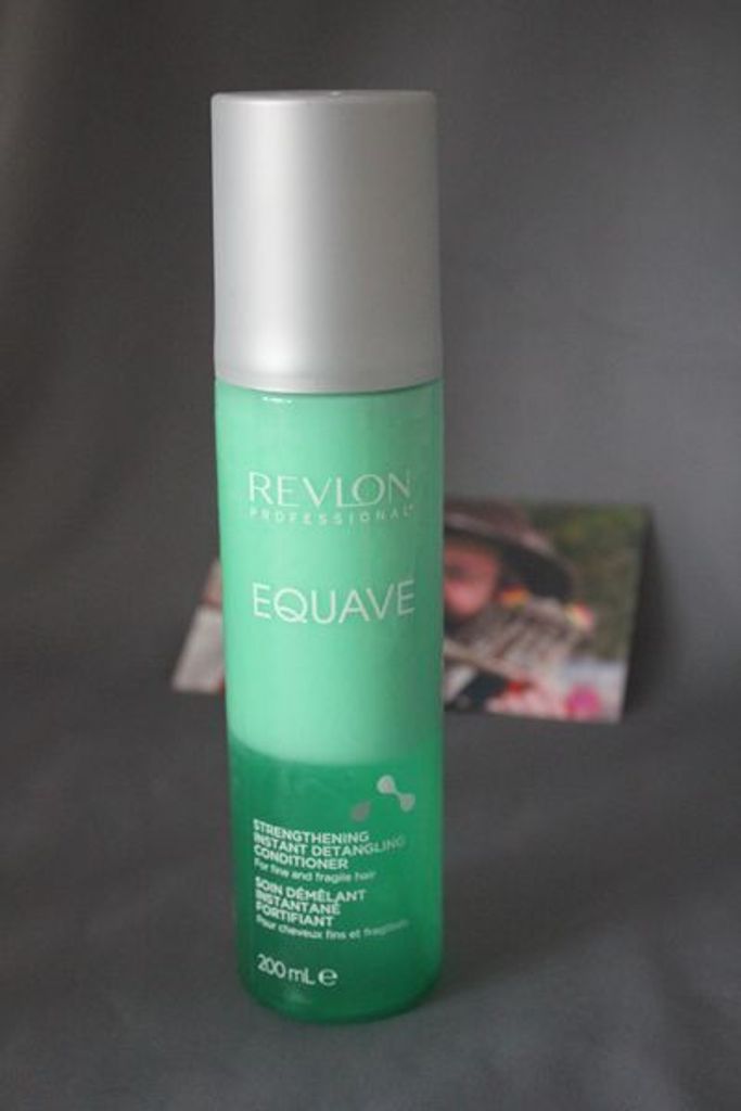 A bottle of Revlon Professional Equave Strengthening Instant Detangling Conditioner is shown against a gray background. A blurred image of a person is visible in the background.