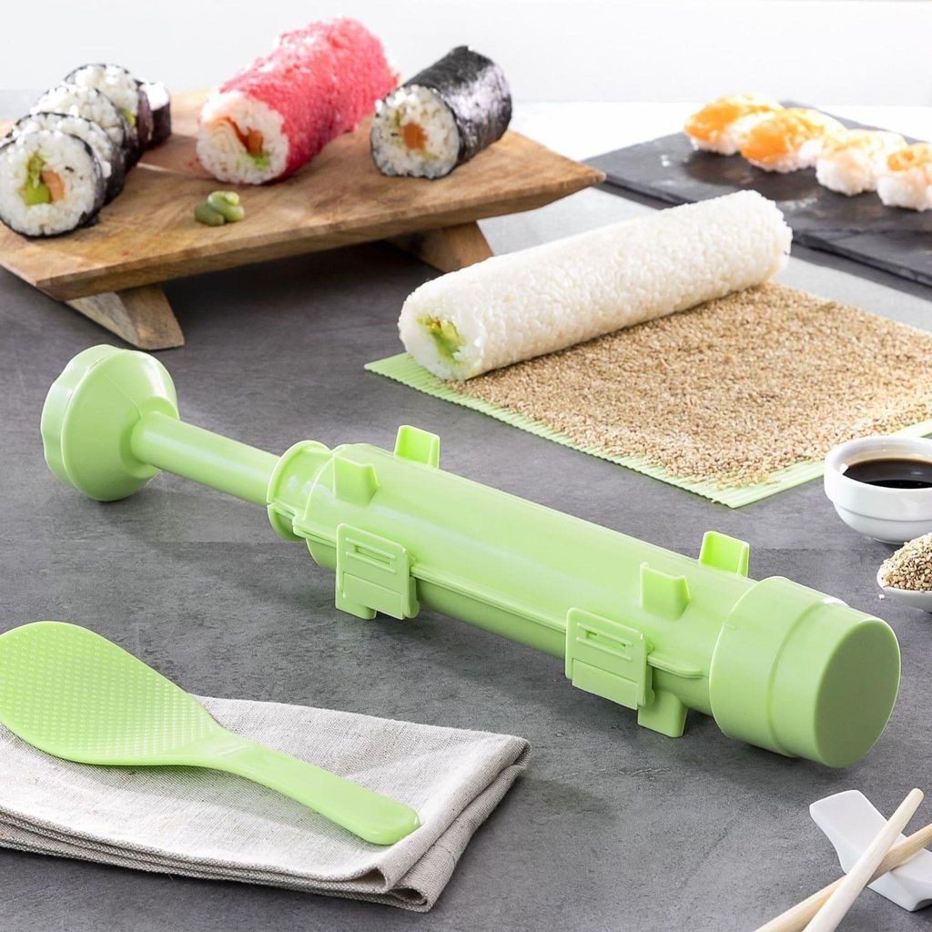 A sushi-making kit is displayed on a countertop, with various sushi rolls and ingredients in the background.