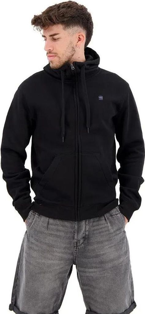 A man wearing a black zip-up hoodie and gray denim shorts, posing against a white background.