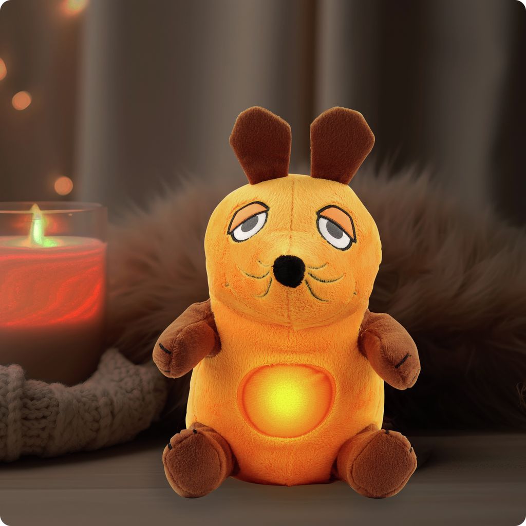 A plush toy mouse with a glowing belly sits on a surface next to a lit candle and fuzzy material.