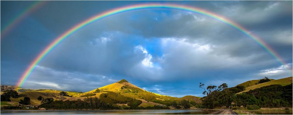Wallario Poster - Regenbogen über Hügel, Kunstdruck Größe: 50 x 125 cm