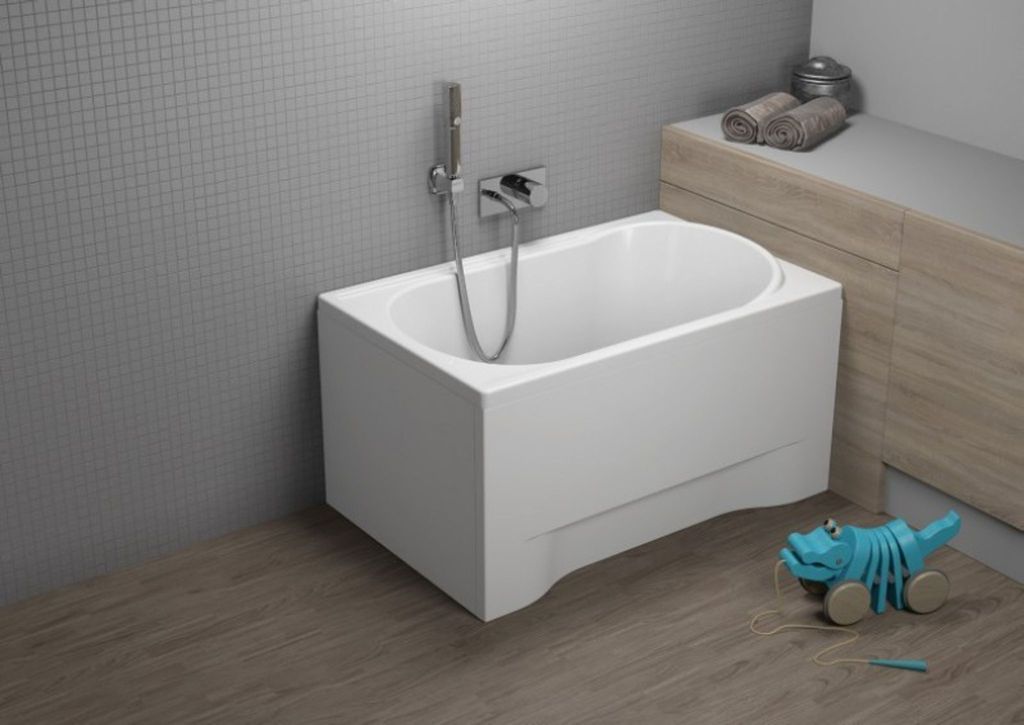 A white bathtub is shown in a bathroom setting with tiled walls and wooden flooring. A blue toy dinosaur is on the floor next to the bathtub.
