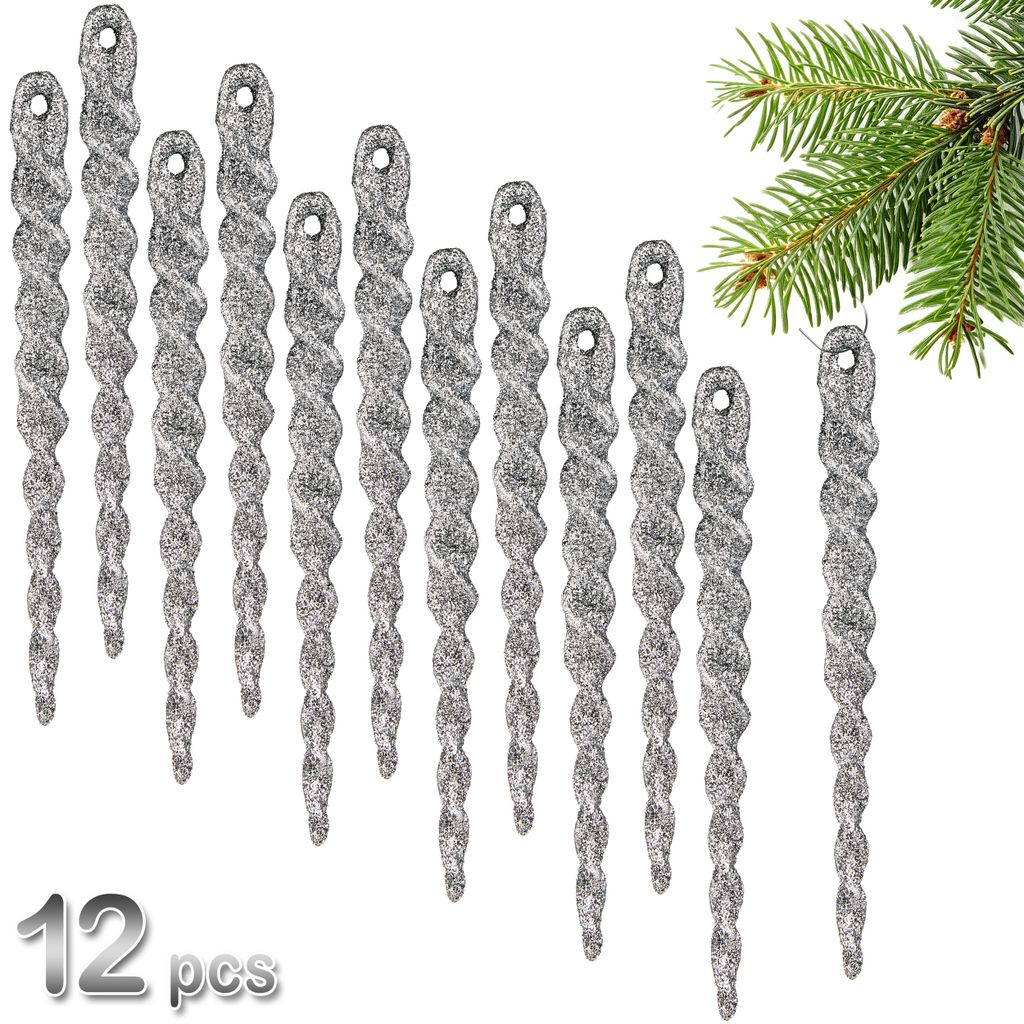 A collection of silver, glittery icicle-shaped Christmas ornaments arranged in a row, with a sprig of a pine tree visible in the upper right corner.