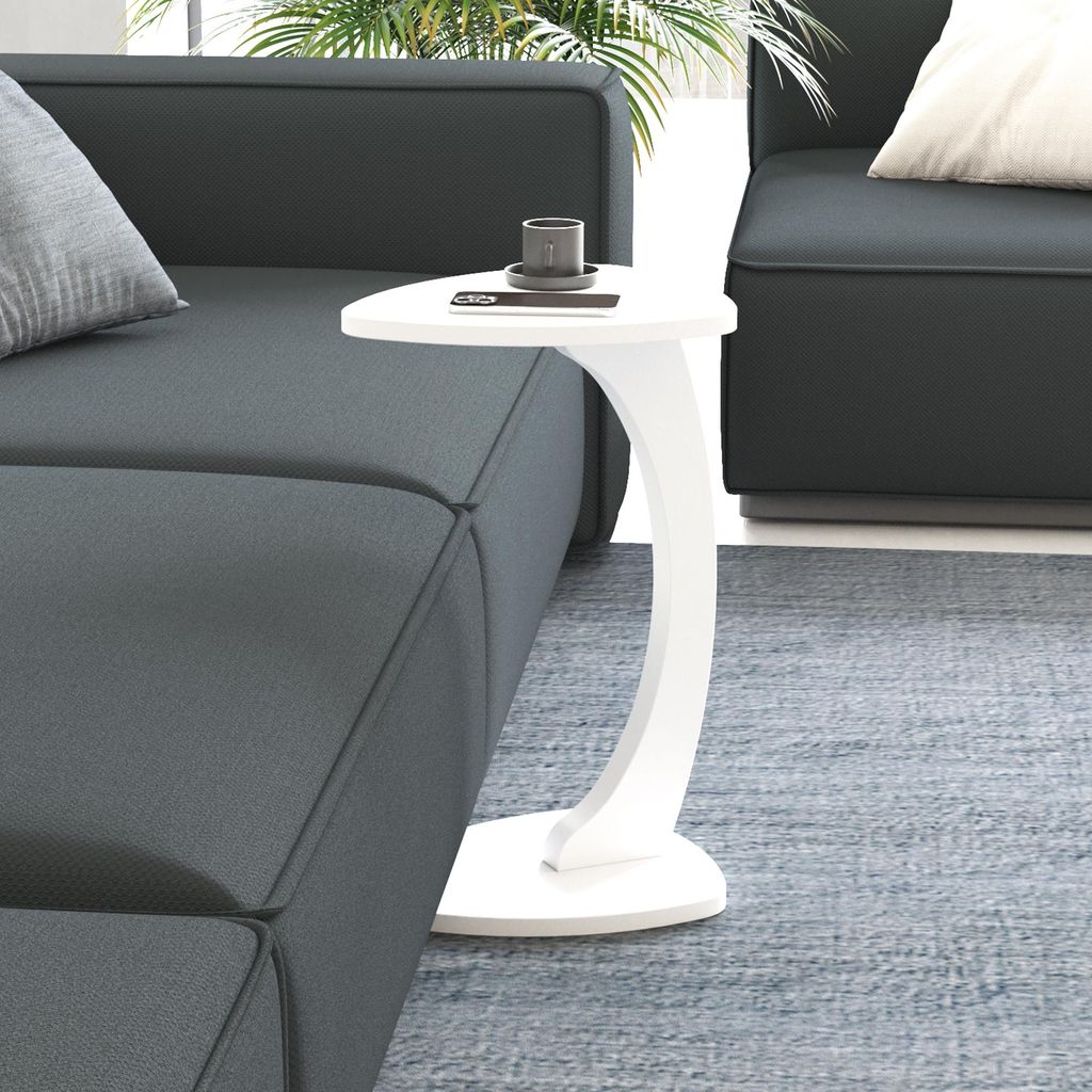 A white C-shaped side table with a cup and a phone on it, placed next to a dark gray sofa.