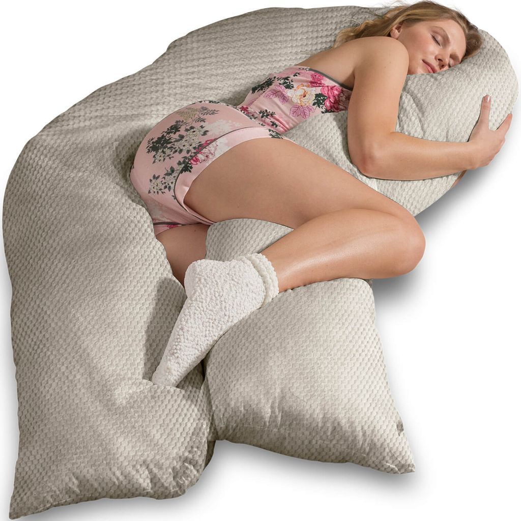 A woman is sleeping on a large, C-shaped pillow.