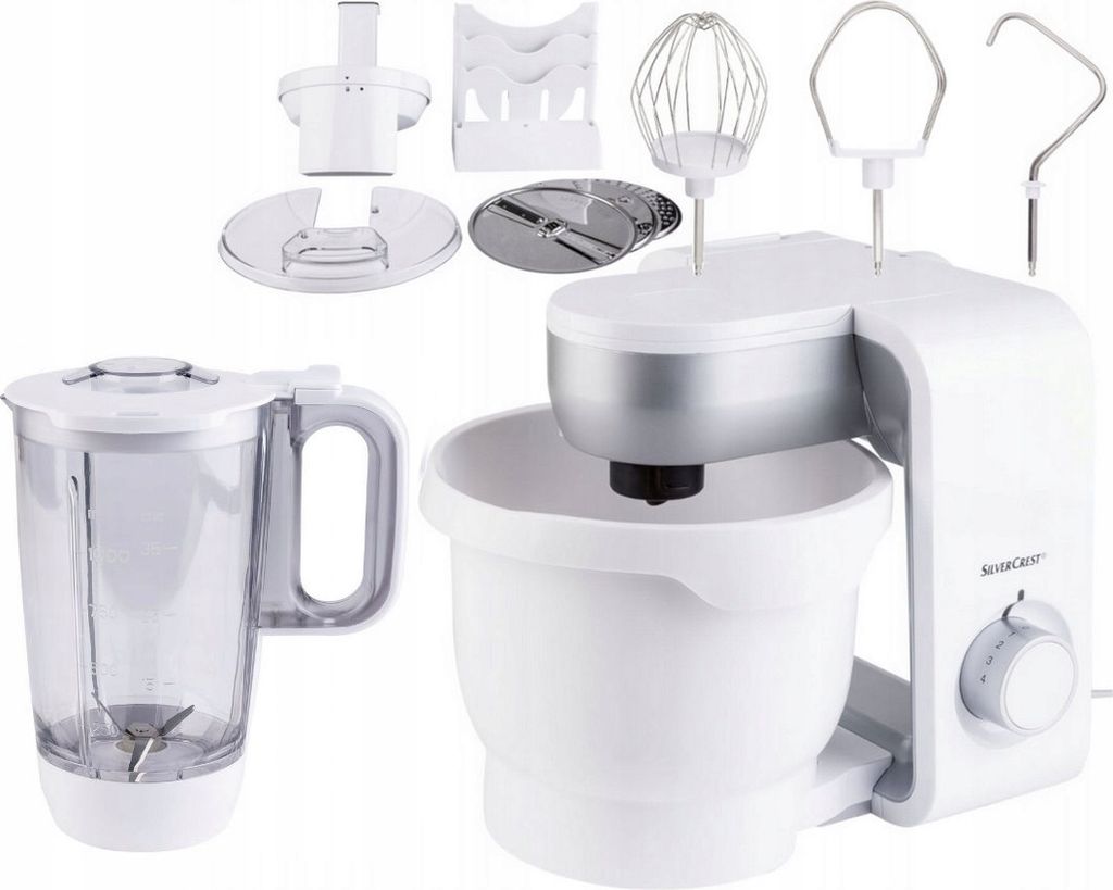 A white Silvercrest kitchen machine with various attachments, including a blender jug, whisk, dough hook, and slicing discs, is displayed against a white background.