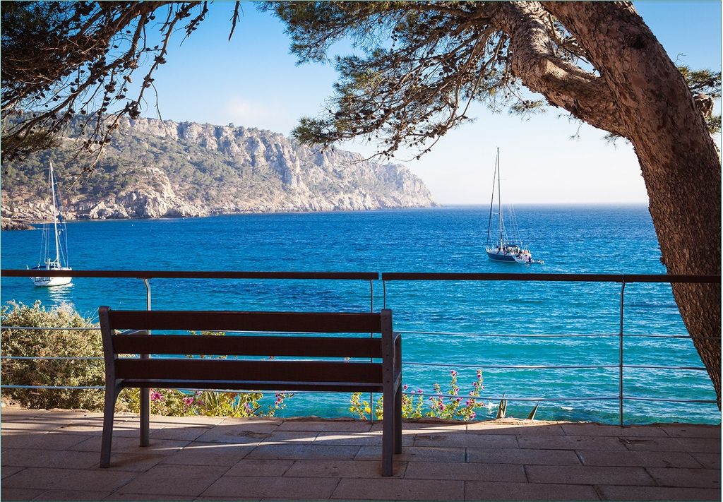Wallario Fototapete Vliestapete, seidenmatte Oberfläche, einfache Verarbeitung, Größe 200 x 140 cm, Motiv Einsame Bank am Meer - Spanien im Sommer