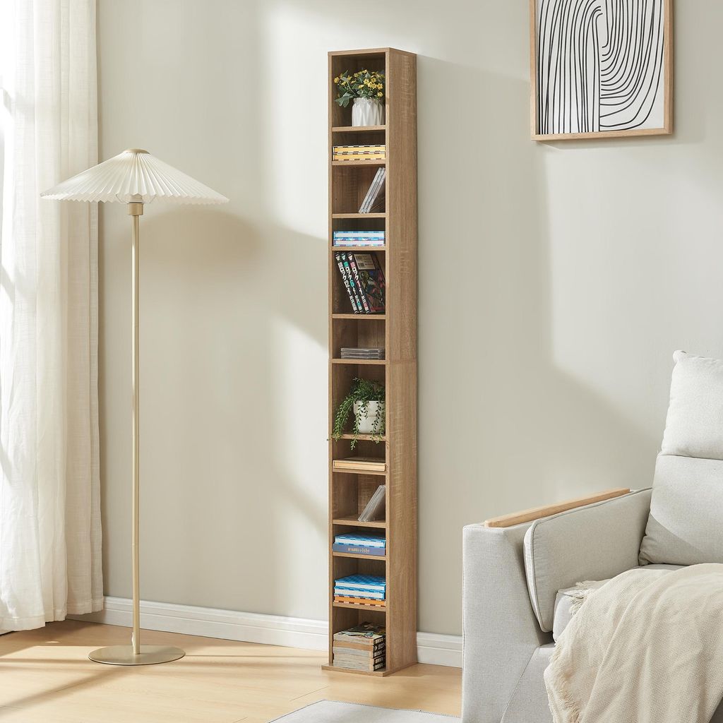 A tall, narrow bookshelf filled with CDs and decorative items stands next to a floor lamp and a sofa in a living room.