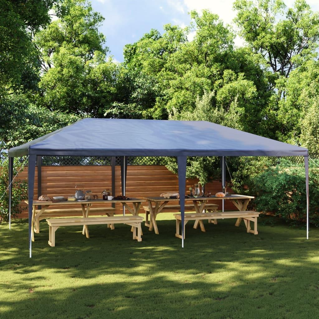 A party tent set up in a backyard with picnic tables underneath.