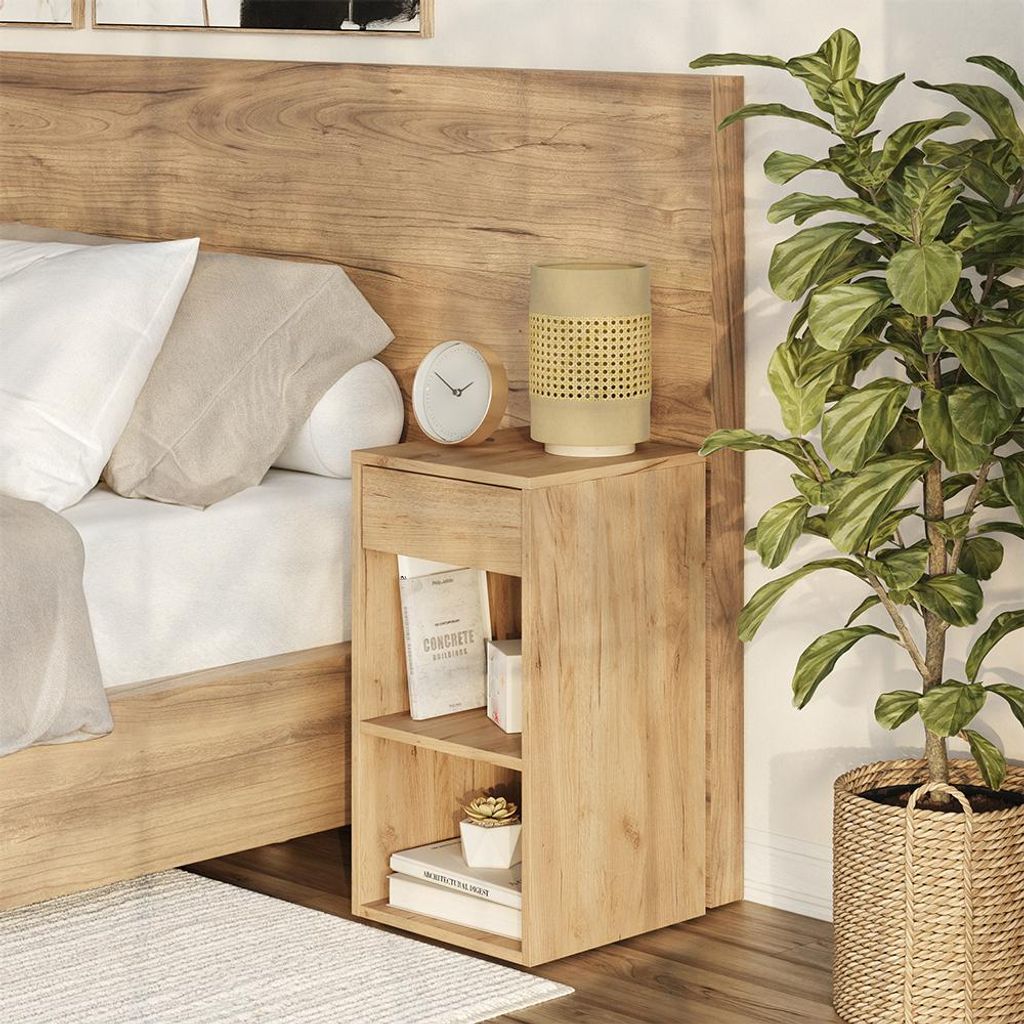 A bedside table next to a bed, with a plant in a basket.