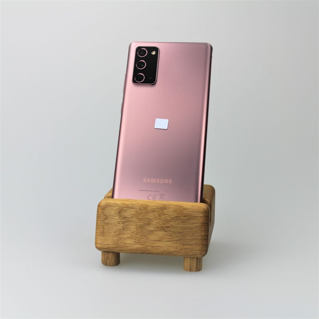 A pink Samsung Galaxy Note20 5G smartphone is displayed in a wooden stand against a white background.