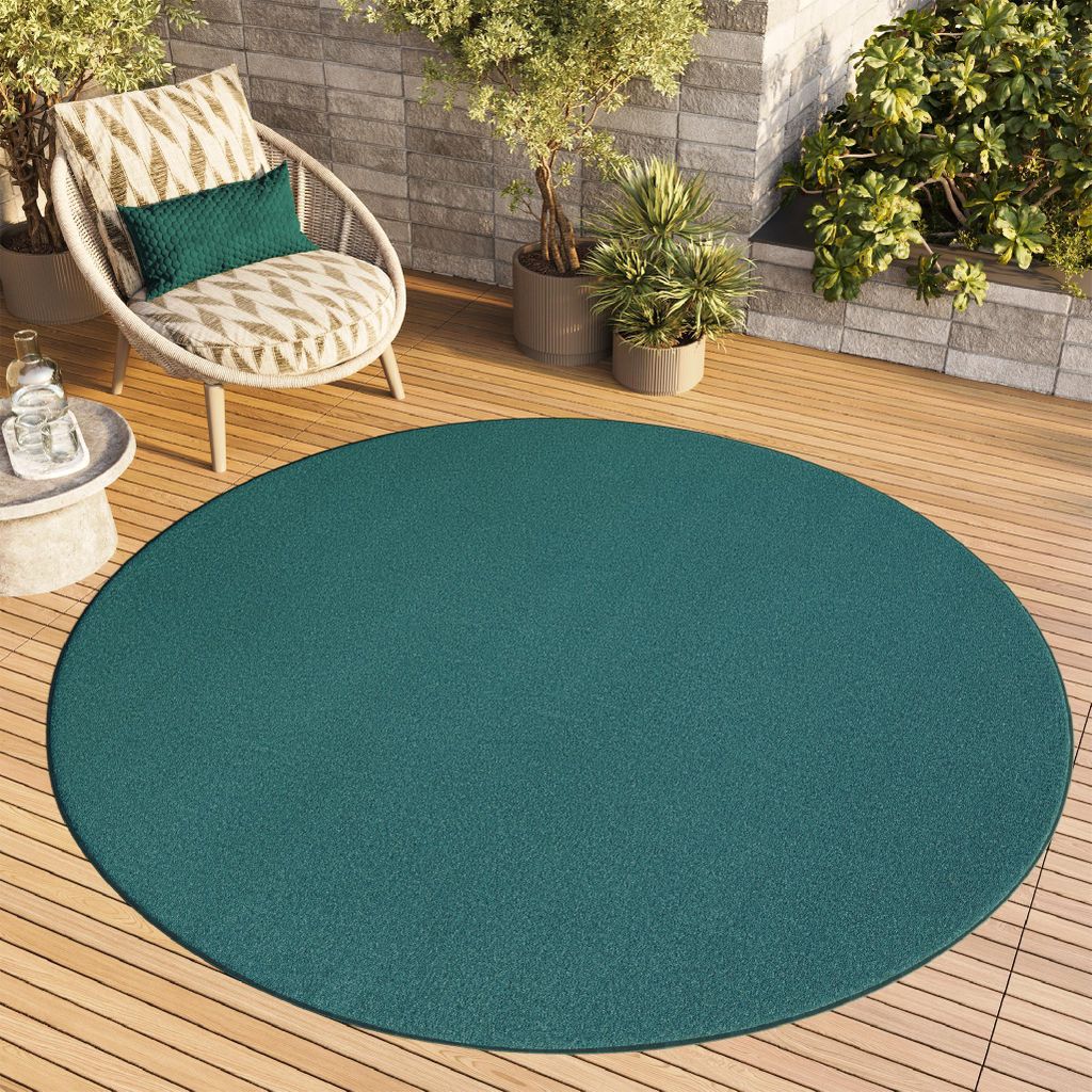 A round teal rug on a wooden deck with a chair and plants.